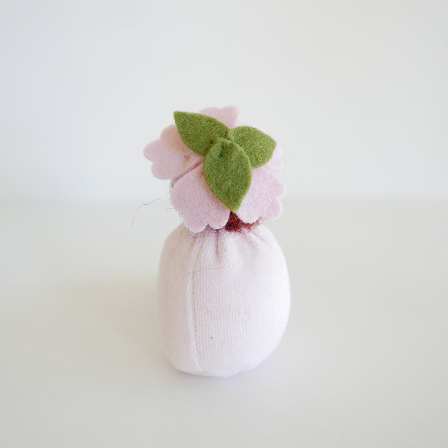 Small pink bath bomb with green leaves on a light gray background