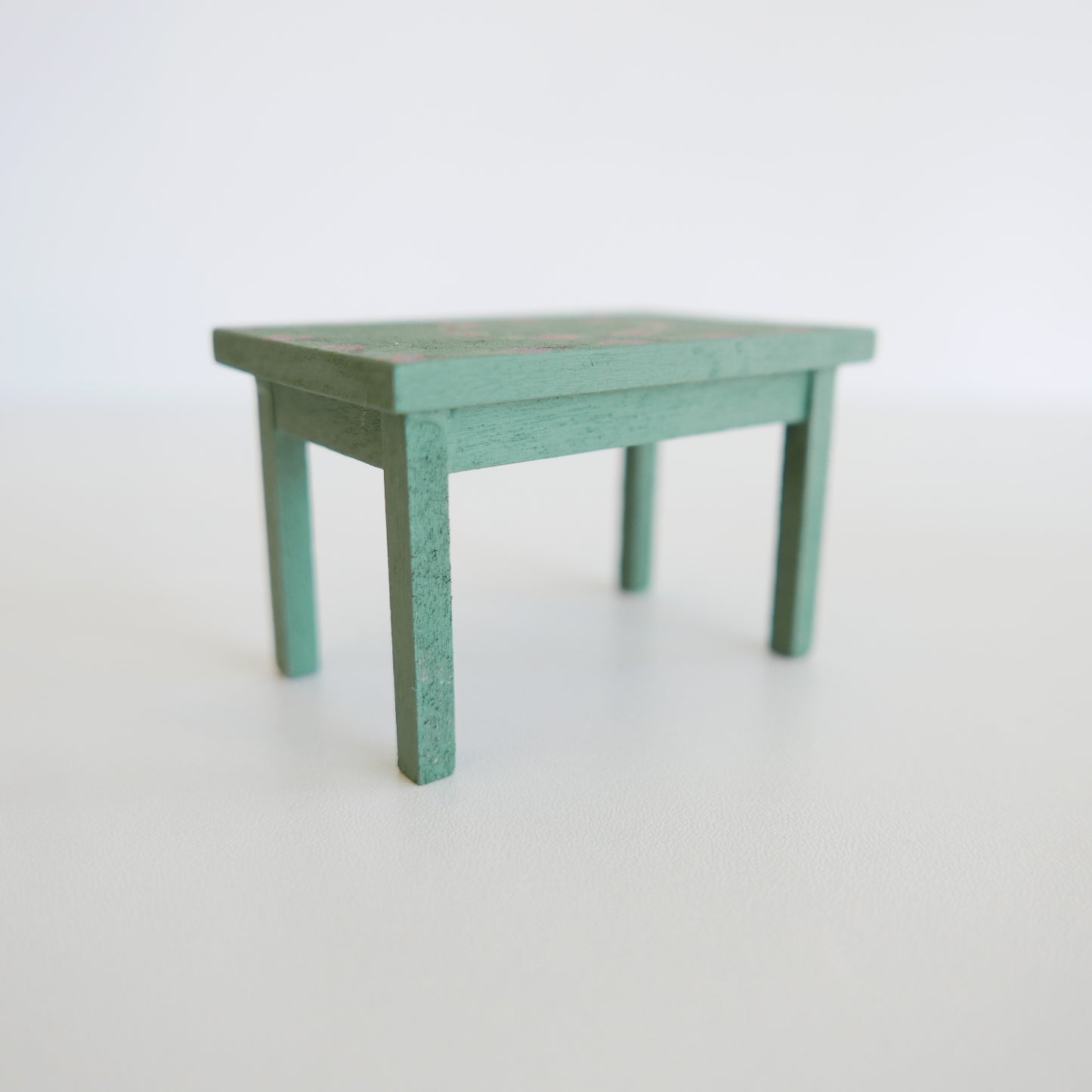 Miniature dining table for dolls house, painted in delicate garden rose pink, displayed on a plain white background