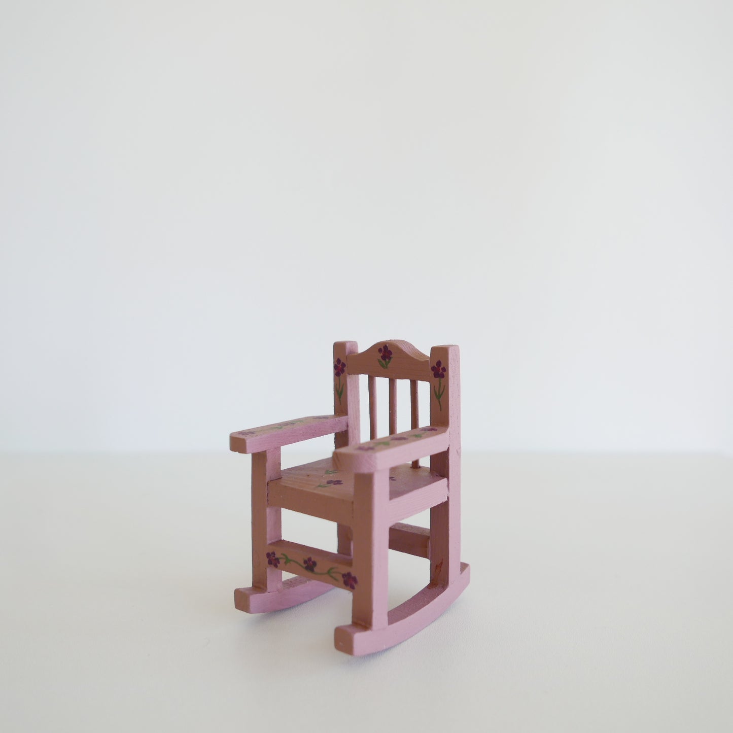 Handcrafted dolls house furniture: small primrose-colored rocking chair with classic spindle back, shown against white