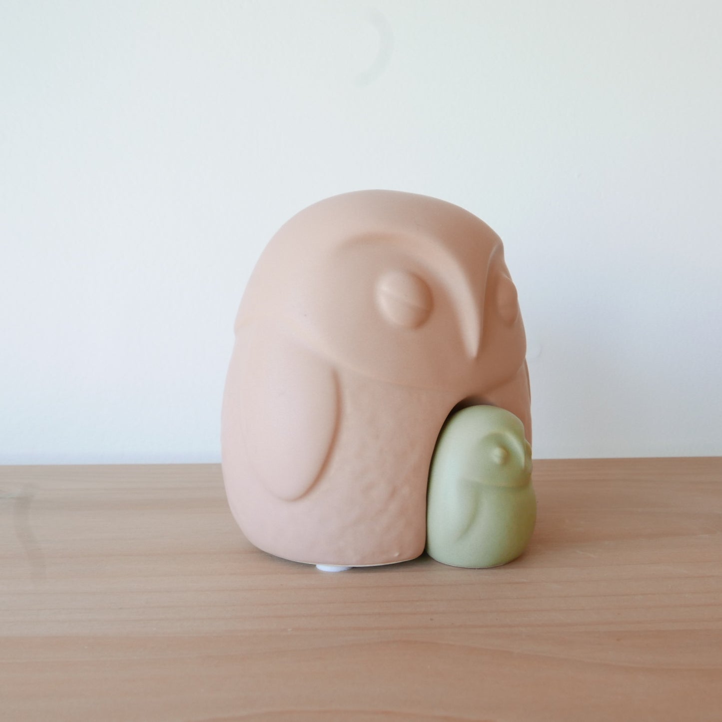 Two ceramic figures, one pink and one green, on a wooden surface with a white background.