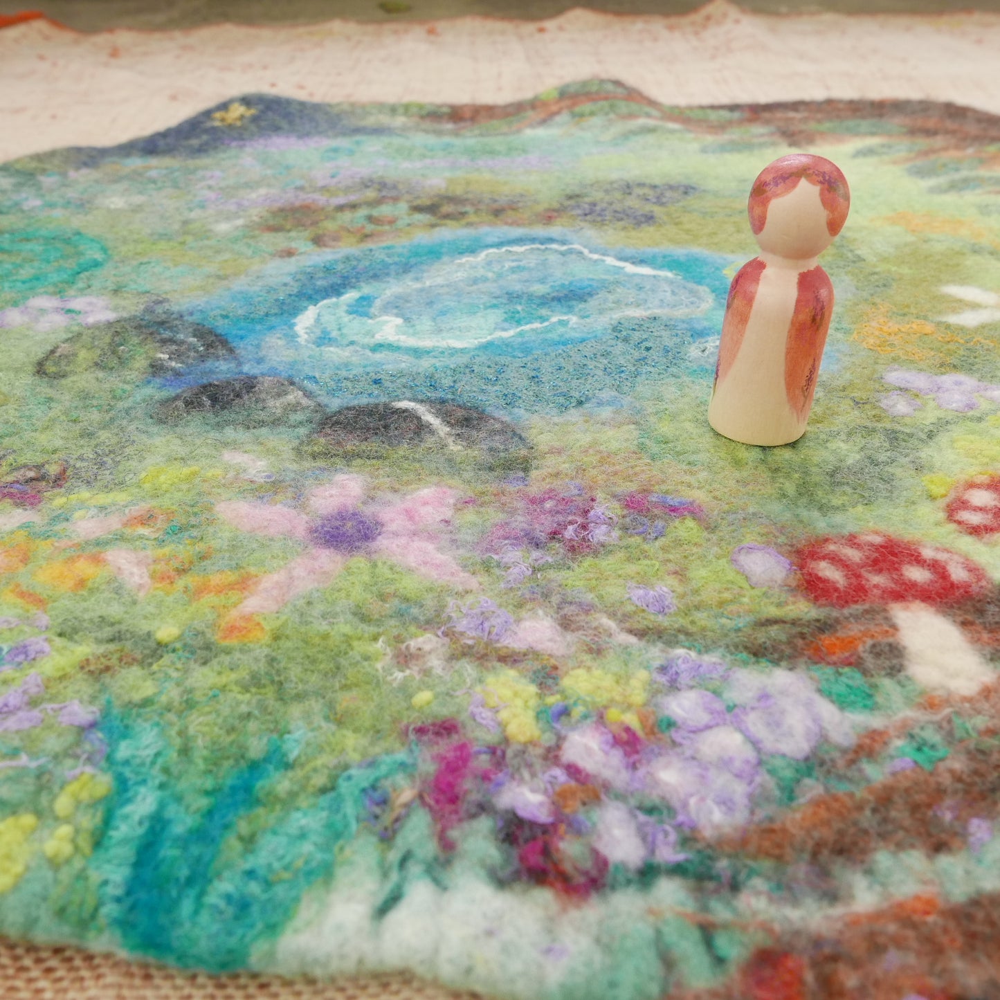 Felted landscape with a small figurine on a textured surface