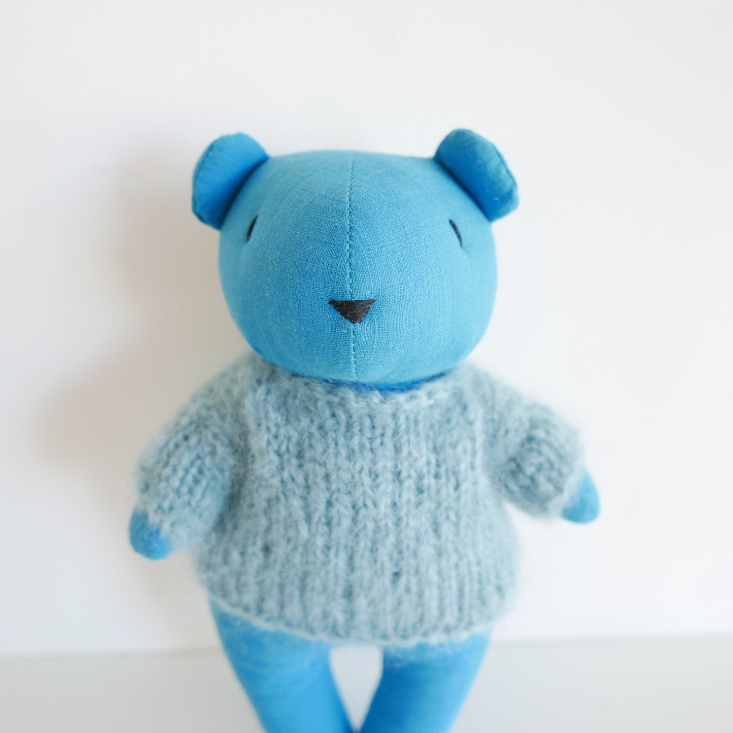 Blue teddy bear wearing a knitted sweater on a white background