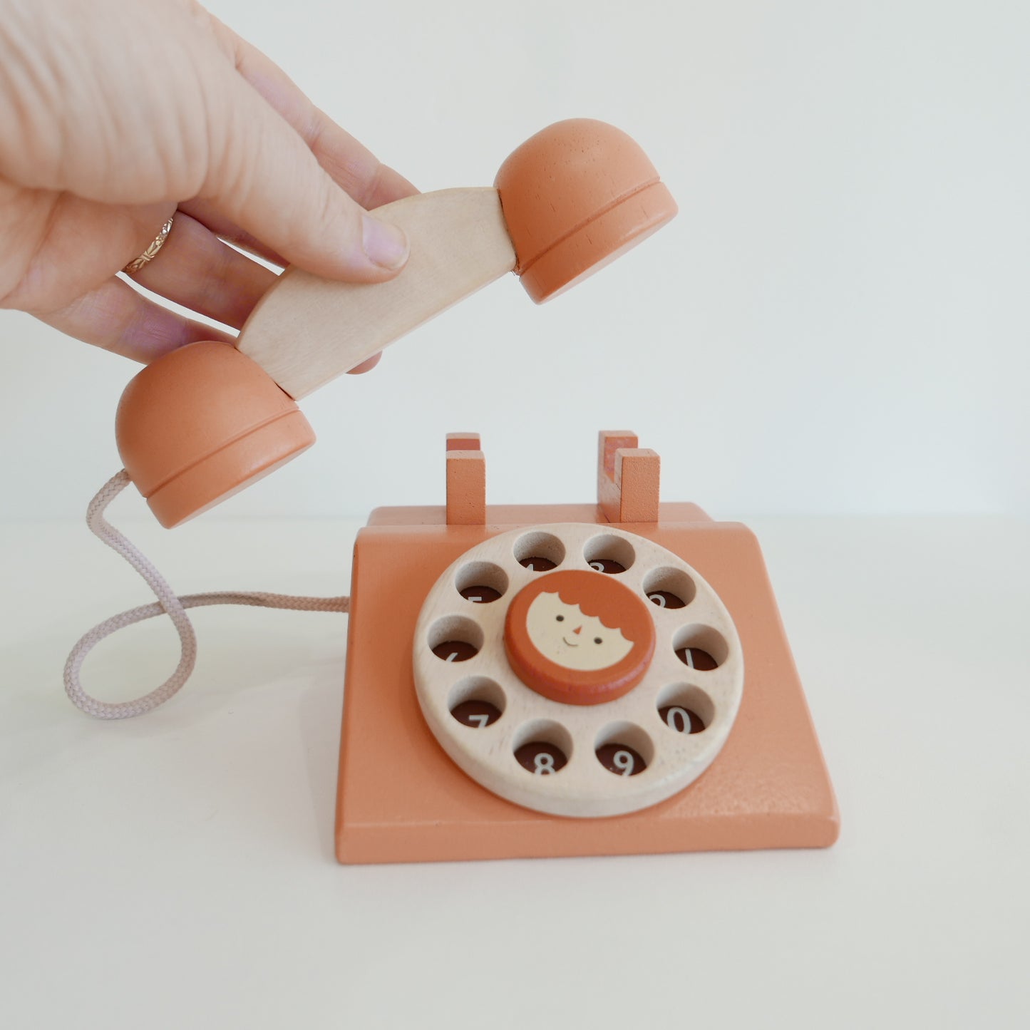 Wooden toy phone with rotary dial held by a hand