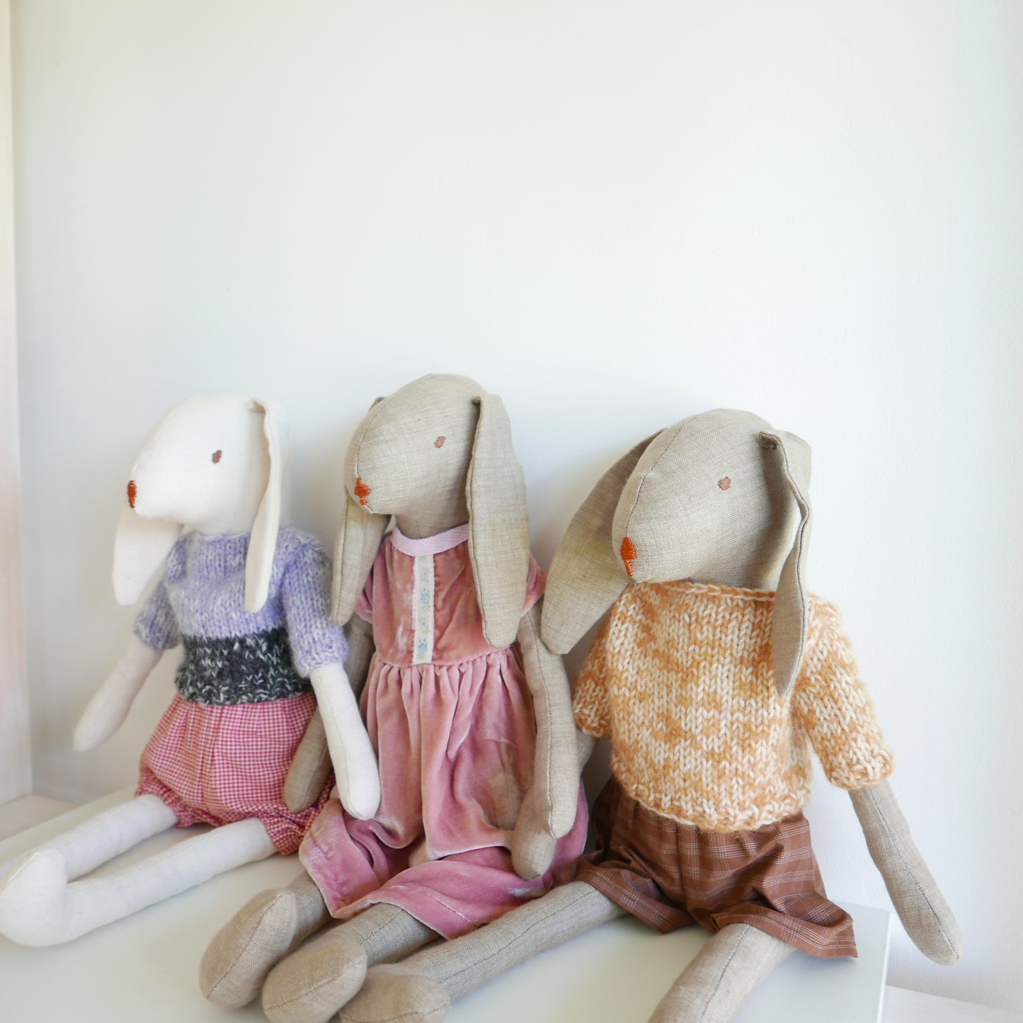 Three stuffed rabbit dolls wearing colorful outfits on a white background