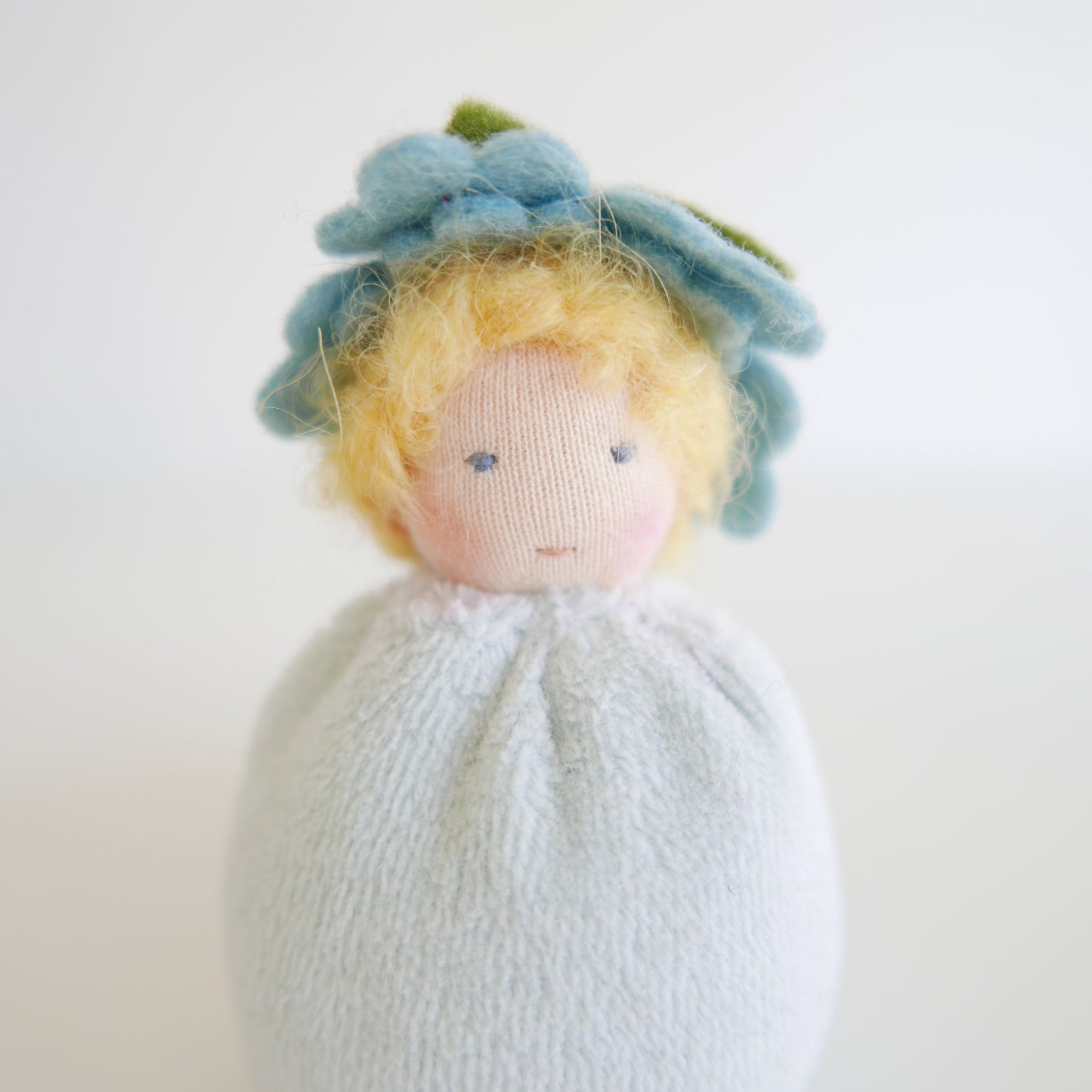 Small doll with yellow hair and a light blue dress on a white background