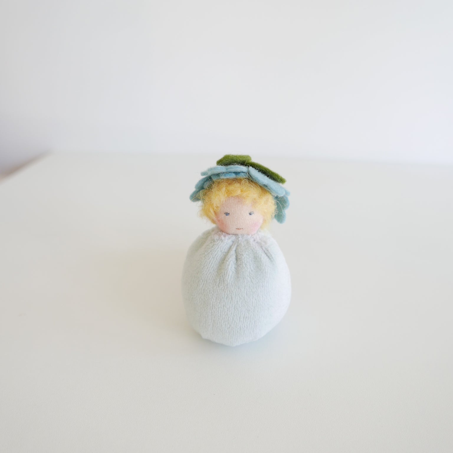 Small plush toy with a green hat and light blue body on a white background