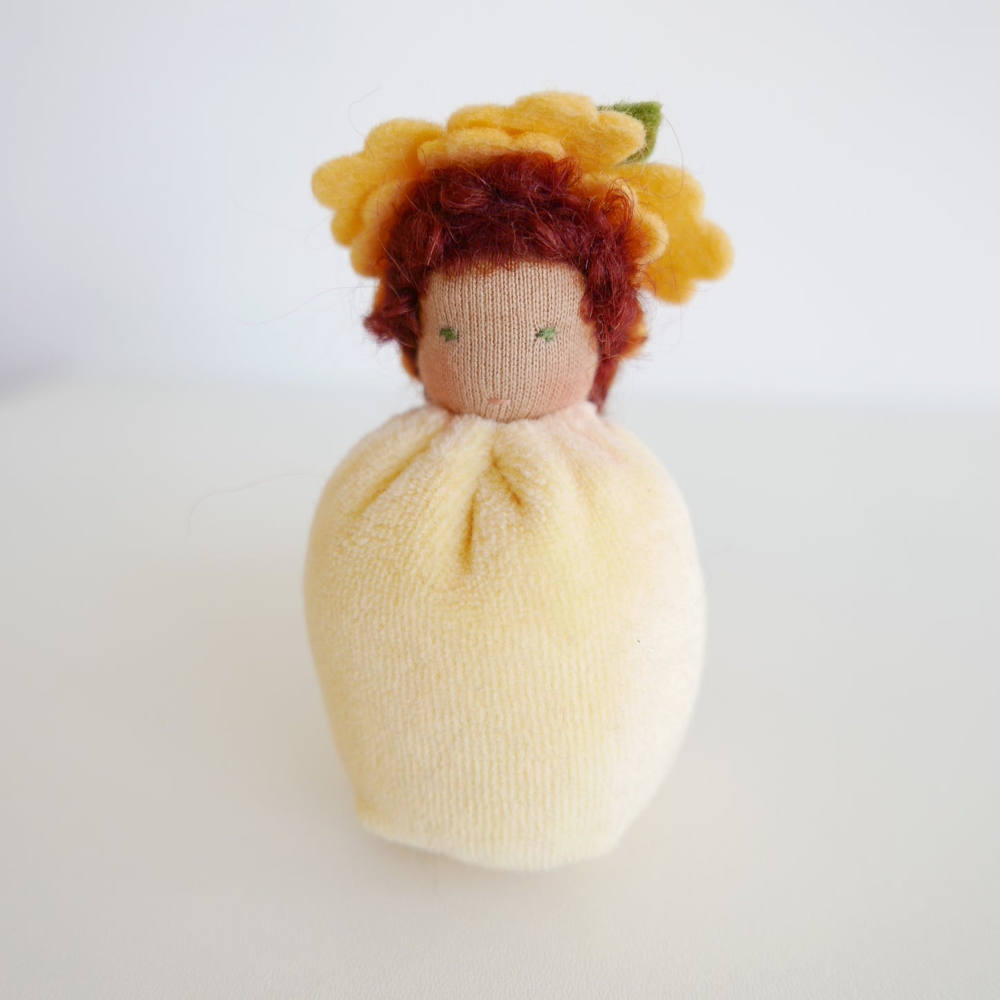 Small doll with yellow hair and a white dress on a light gray background