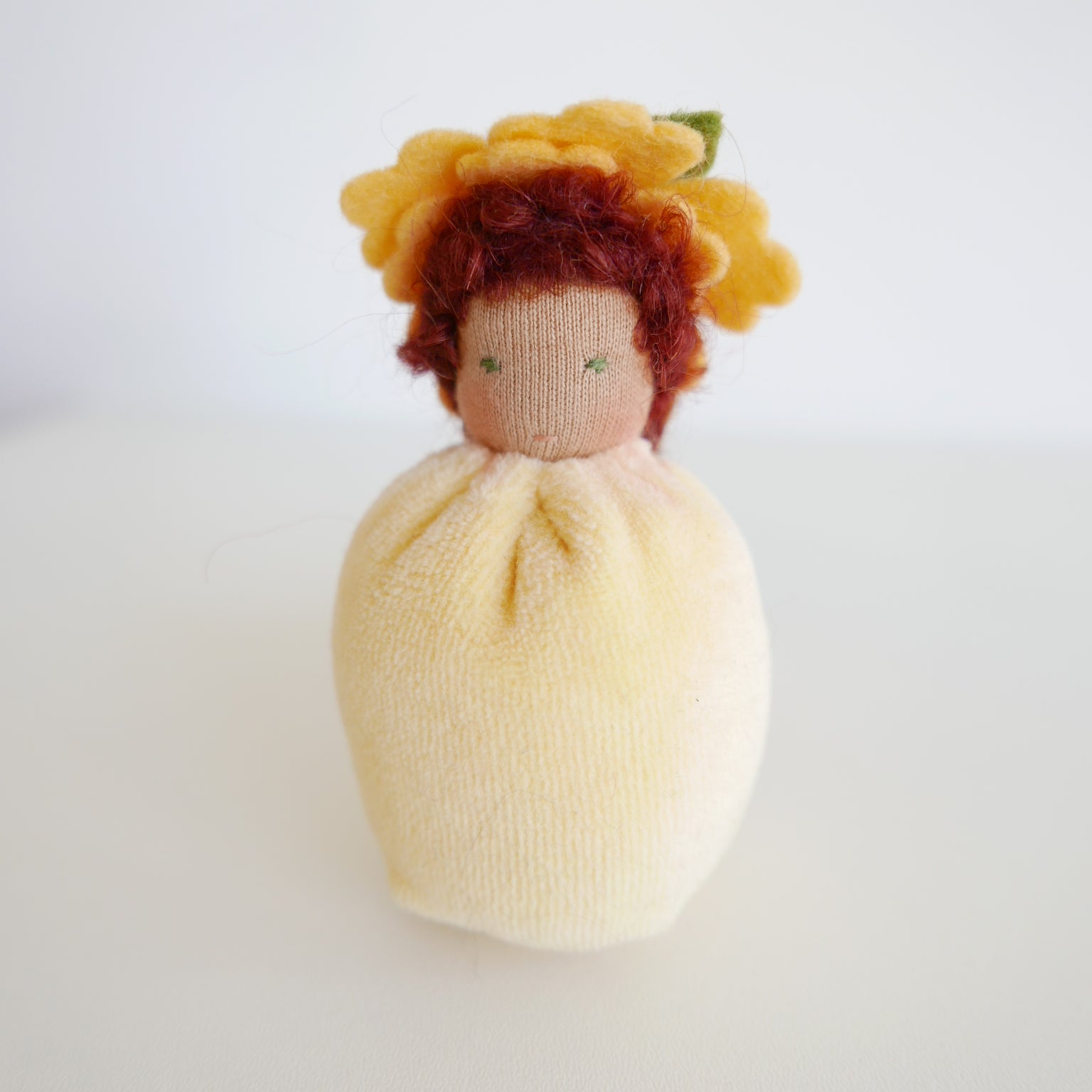 Small doll with yellow hair and a white dress on a light gray background