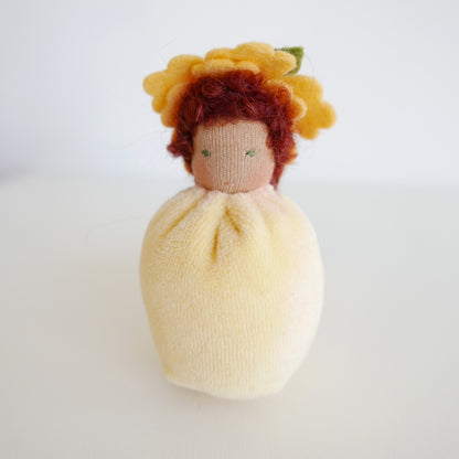 Small doll with yellow hair and a white dress on a light gray background