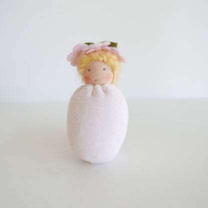 Small doll with a white dress and yellow hair on a light gray background