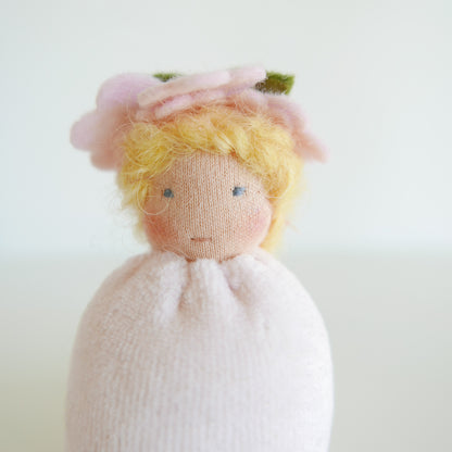 Close-up of a small doll with yellow hair and pink clothing on a light background