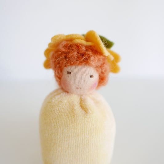 Small doll with yellow hair and a white dress on a light background