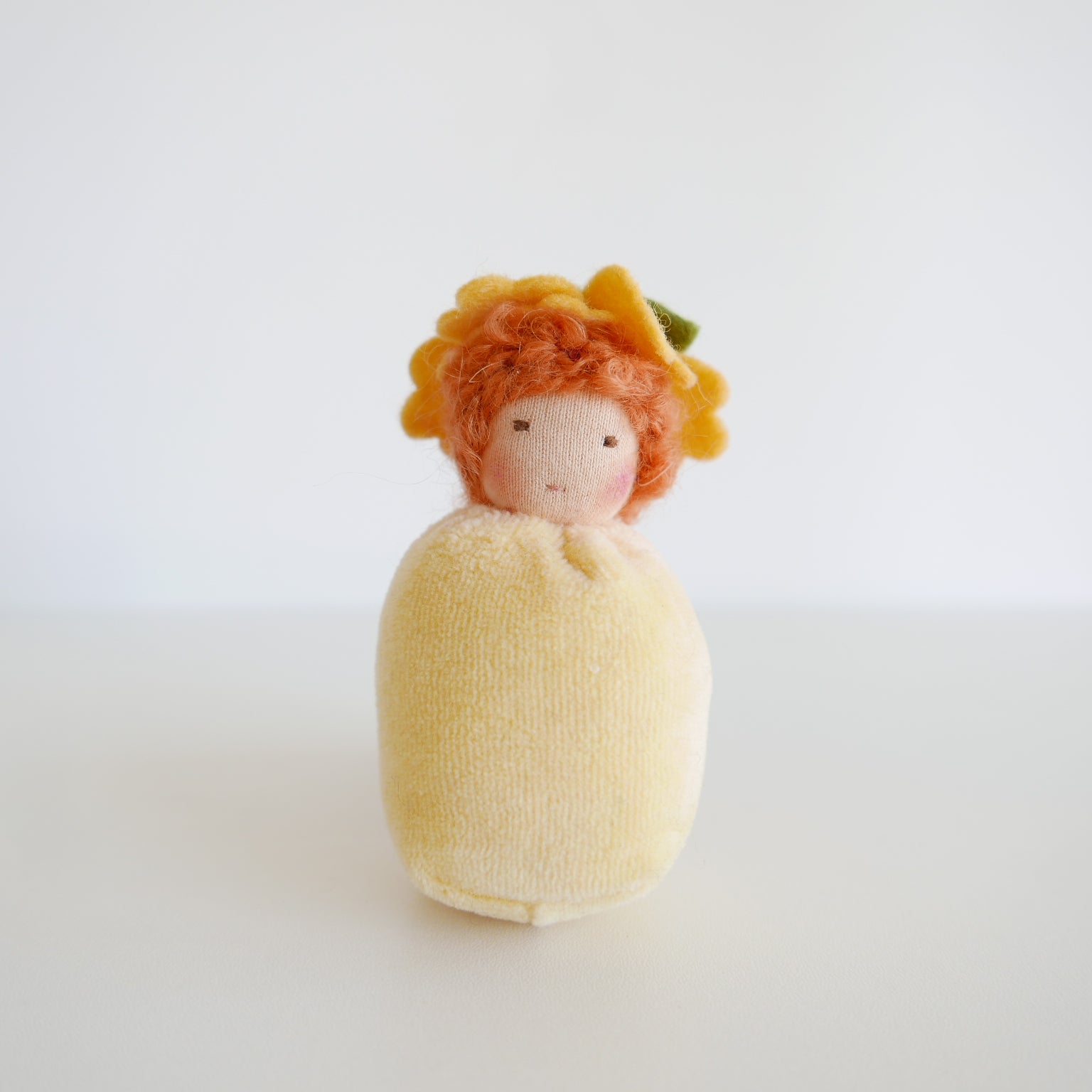 Small doll with orange hair and a yellow dress on a white background