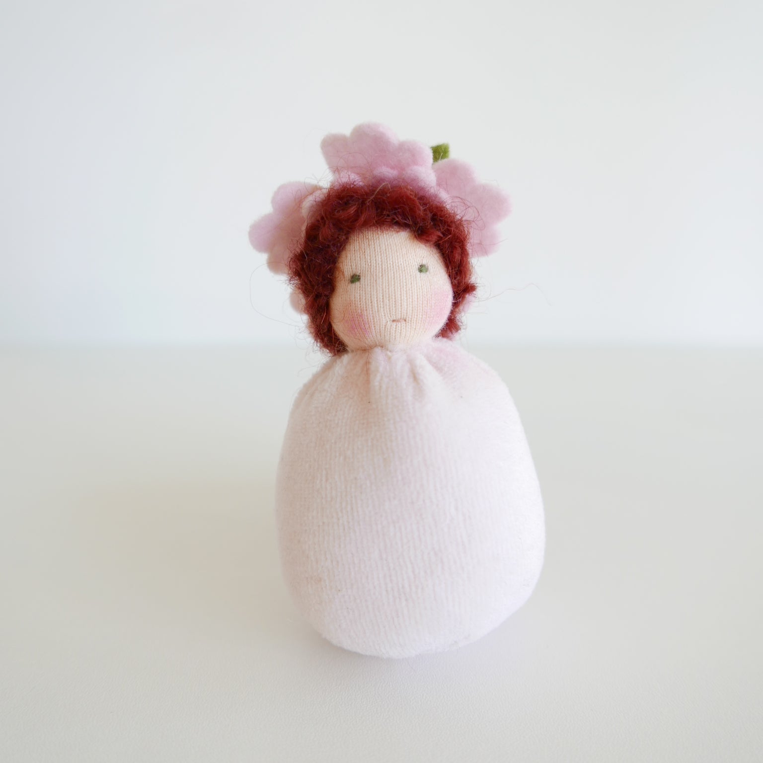 Knitted doll with red hair and a white dress on a light background