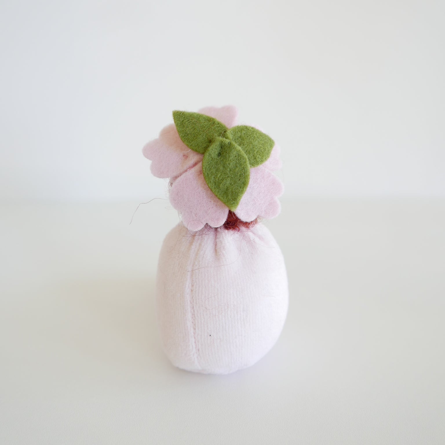 Small pink bath bomb with green leaves on a light gray background