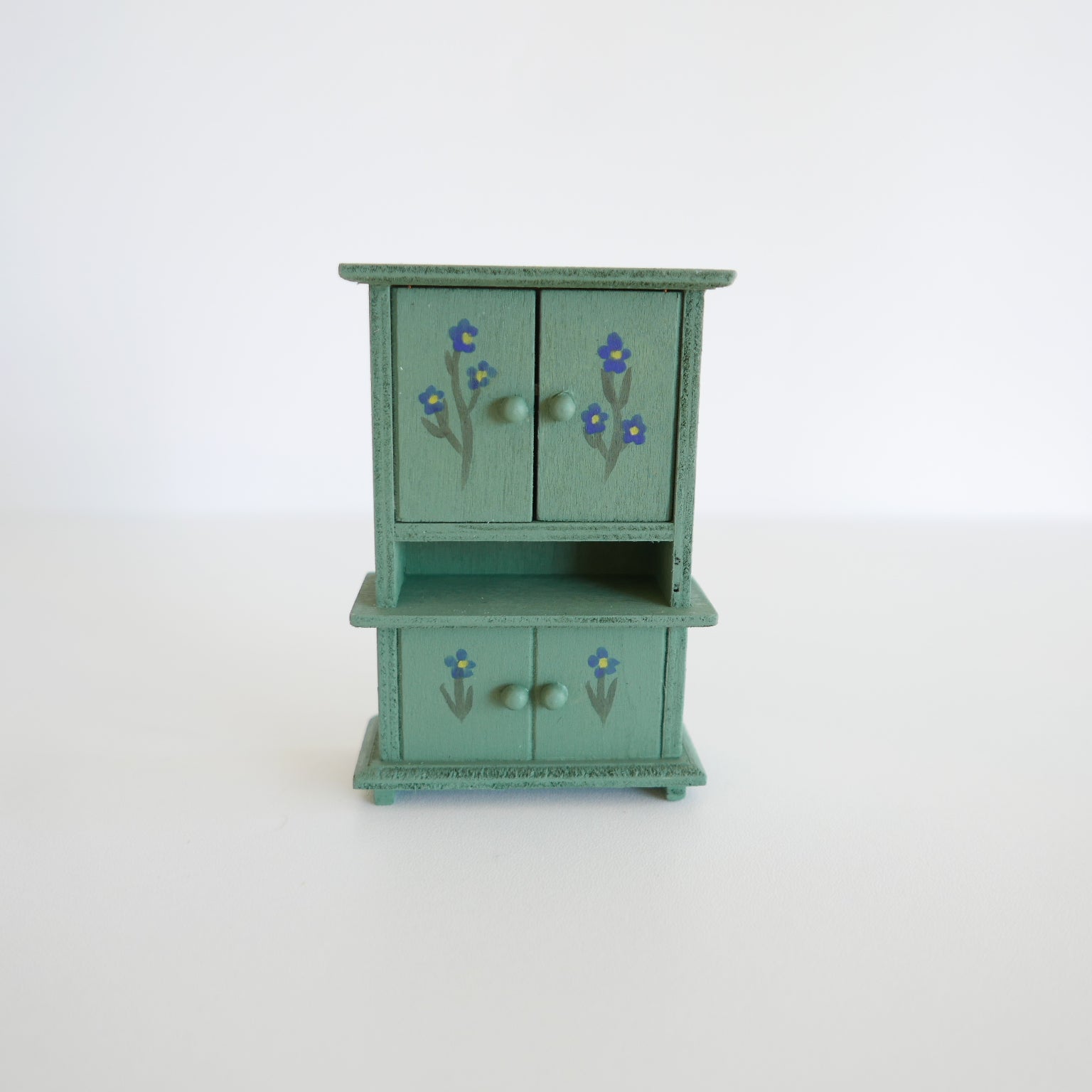 Small green wooden cabinet with floral designs on a white background