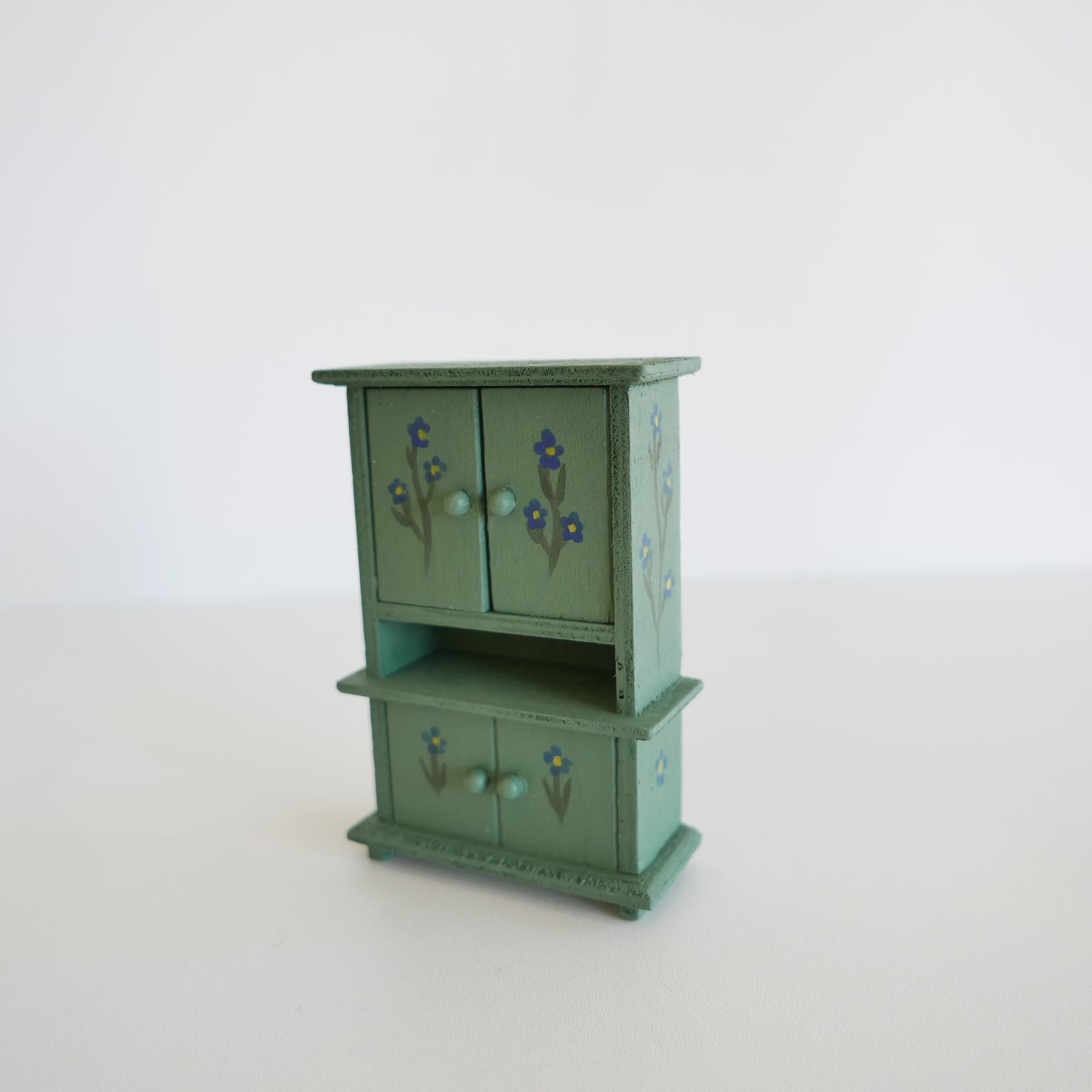 Green miniature wooden cabinet with floral designs on a white background
