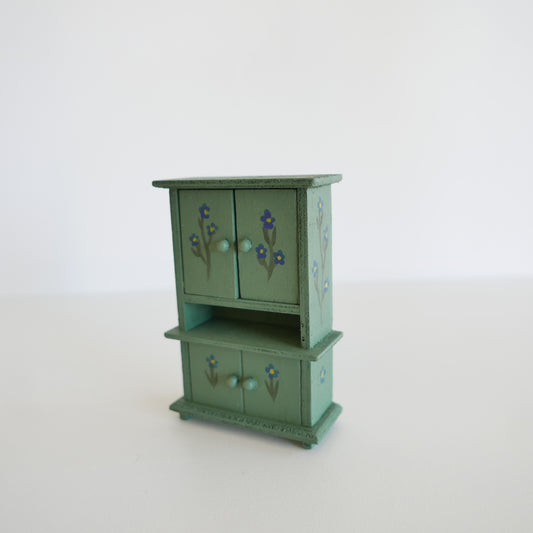 Green miniature wooden cabinet with floral designs on a white background