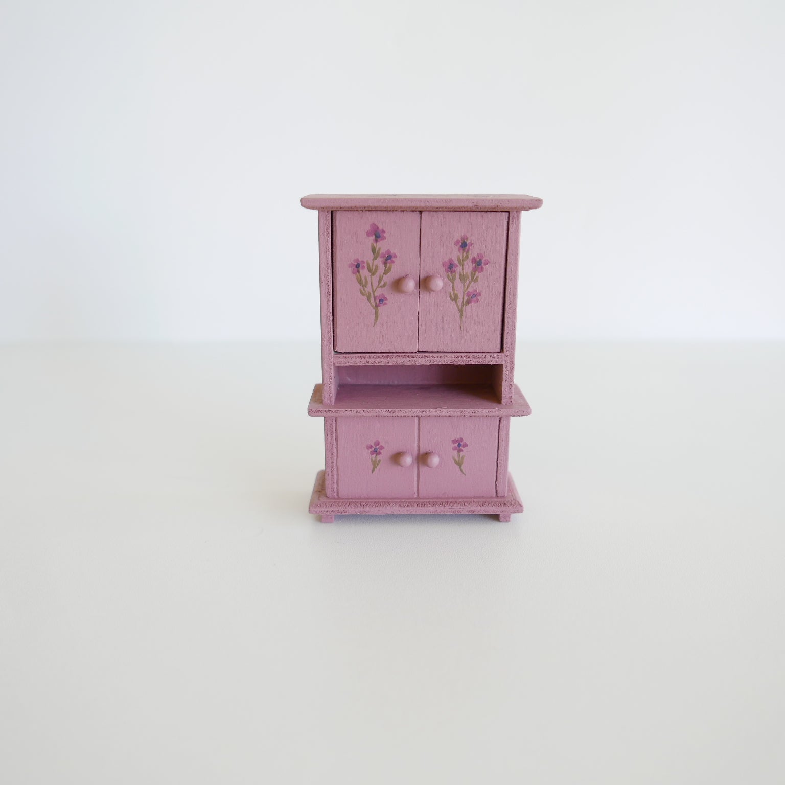 Small pink wooden cabinet with floral designs on a white background