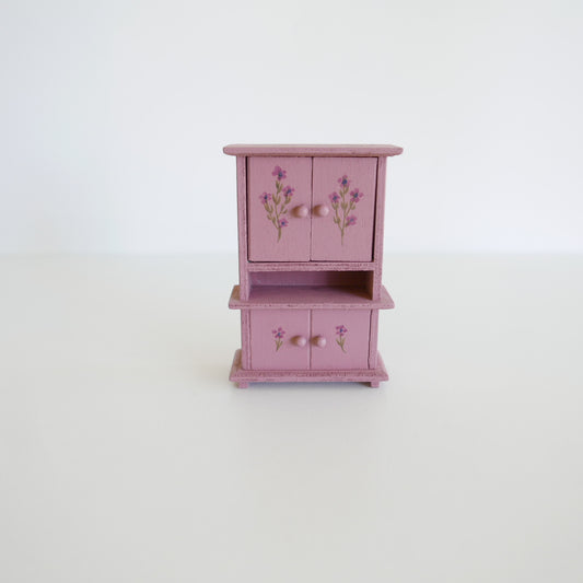 Small pink wooden cabinet with floral designs on a white background