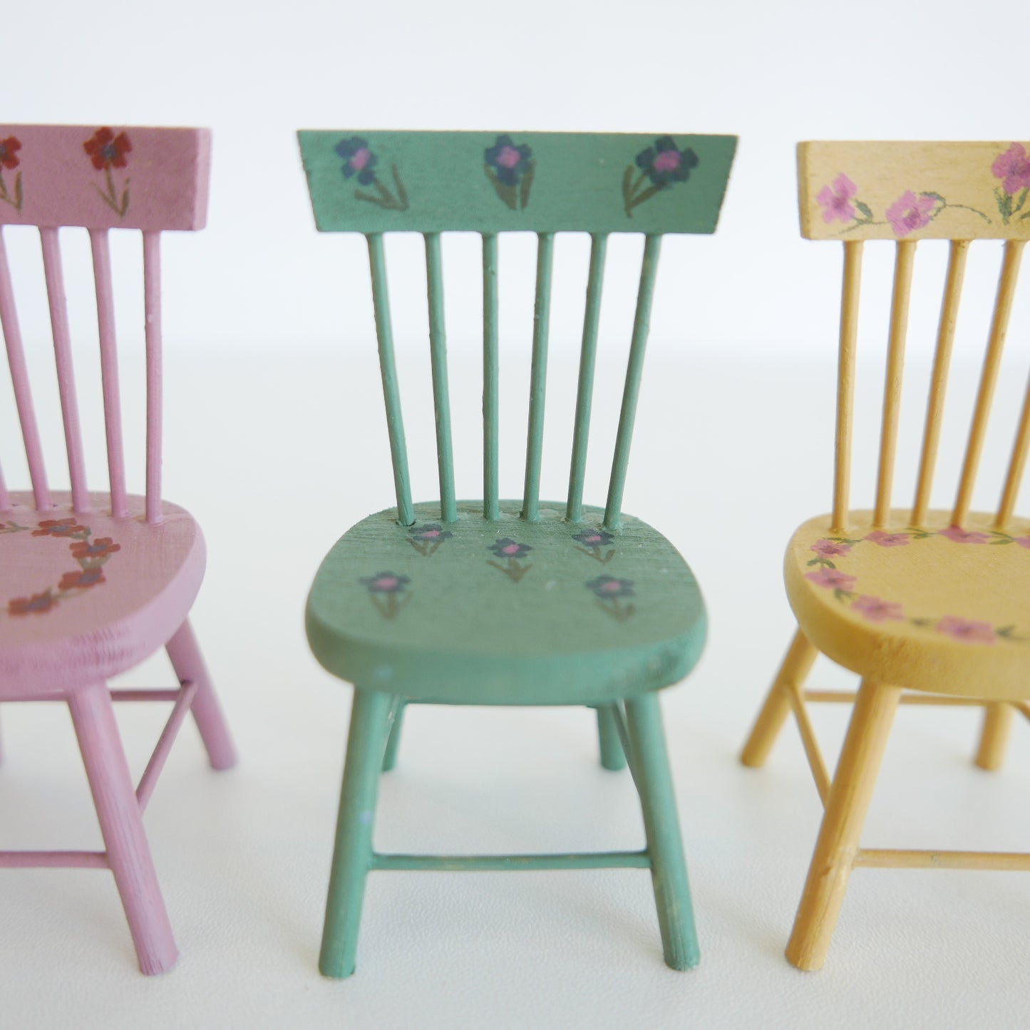 Handcrafted dolls house furniture: small cream-colored dining chair with classic spindle back, shown against white