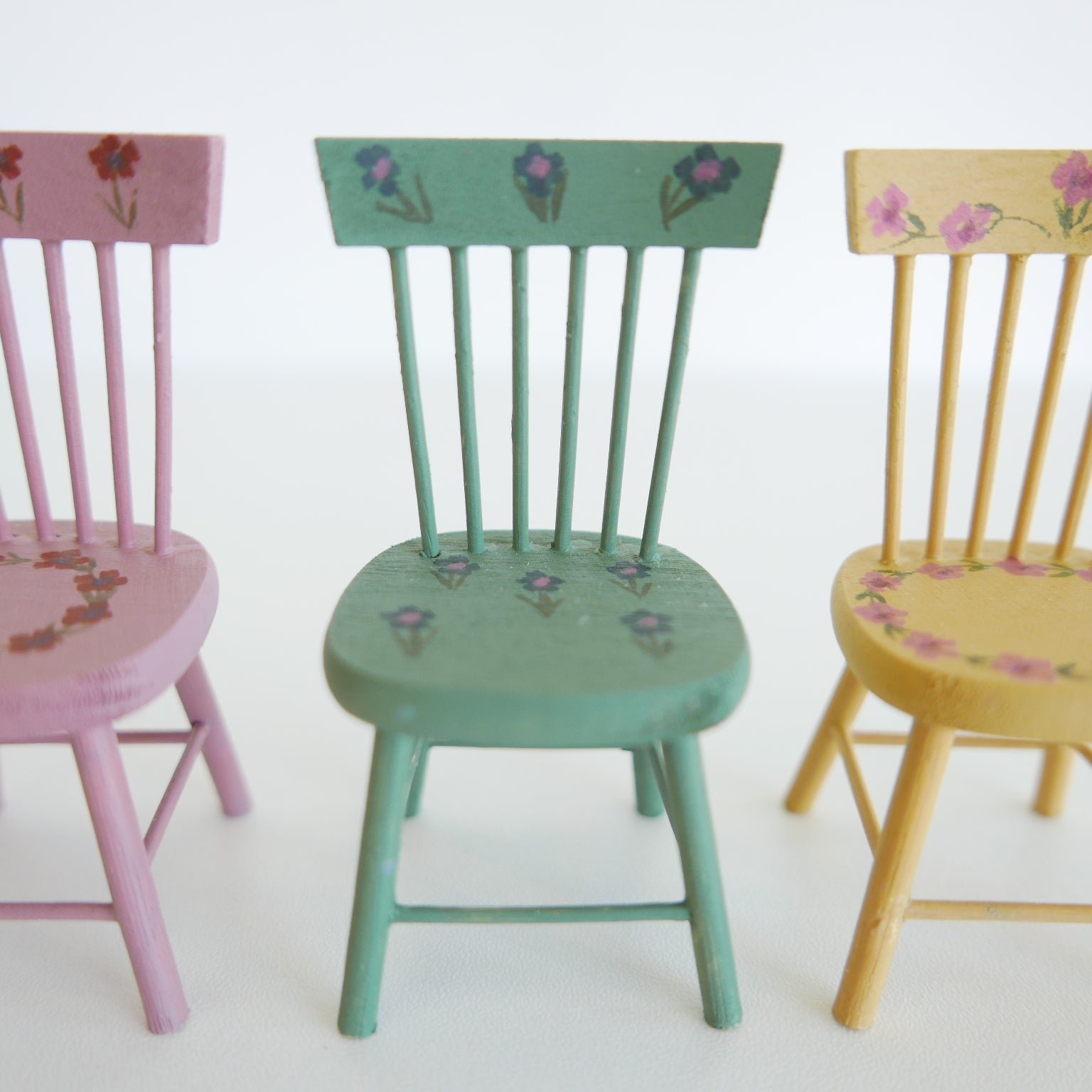 Handcrafted dolls house furniture: small cream-colored dining chair with classic spindle back, shown against white