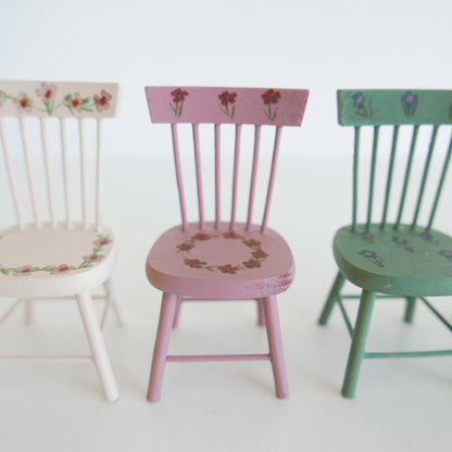 Three wooden chairs in pastel colors with floral patterns on a white background