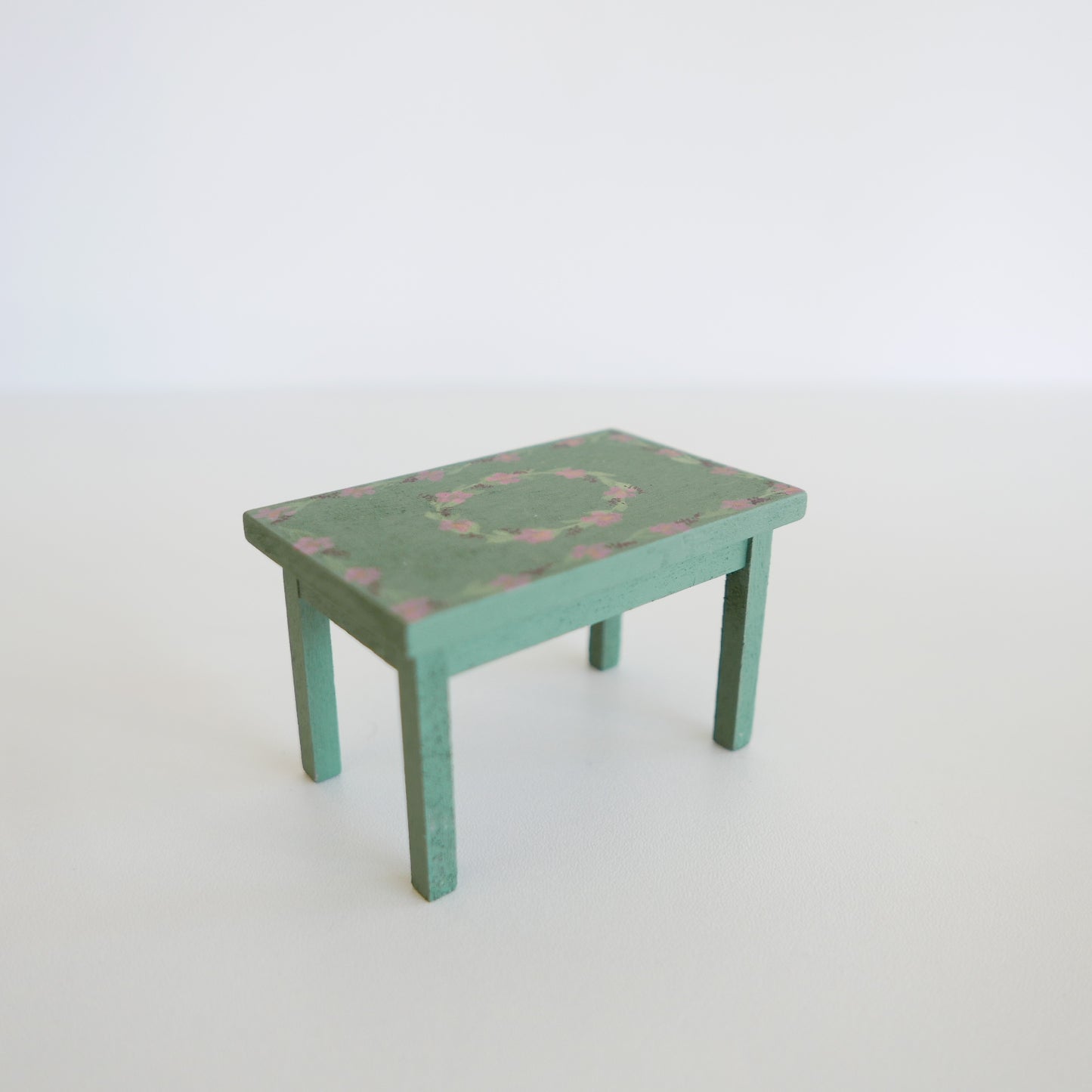 Handcrafted dolls house furniture: small rose-colored dining table with classic rectangular design, shown against white