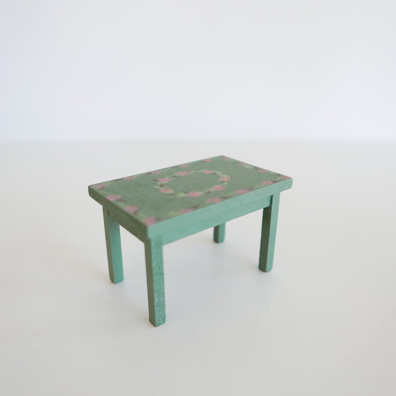 Handcrafted dolls house furniture: small rose-colored dining table with classic rectangular design, shown against white