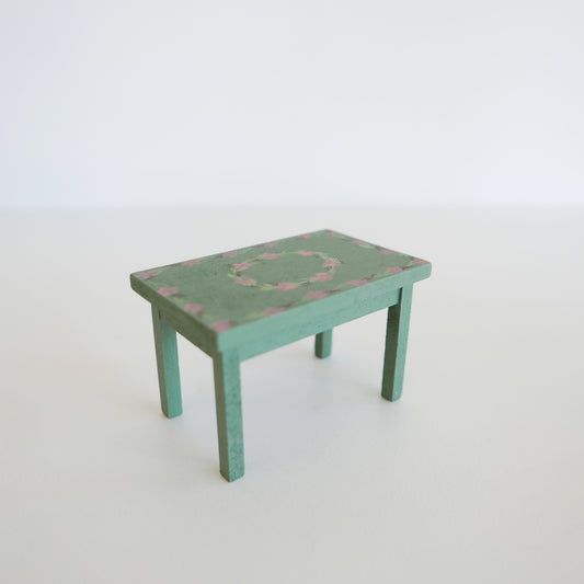 Handcrafted dolls house furniture: small rose-colored dining table with classic rectangular design, shown against white
