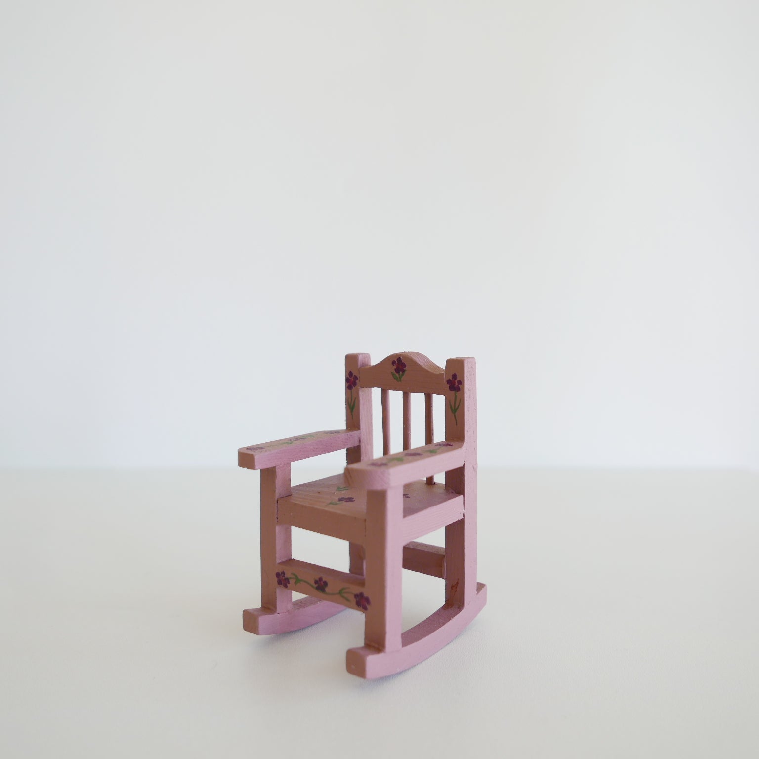 Handcrafted dolls house furniture: small primrose-colored rocking chair with classic spindle back, shown against white