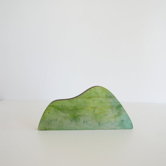 Miniature wooden grassy hill for play scenes or dolls houses, painted in vibrant green tones, isolated on white