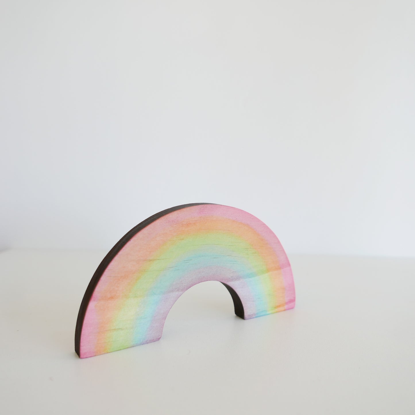 Wooden rainbow stacker in soft pastel colors, arranged in an arch on a plain white background