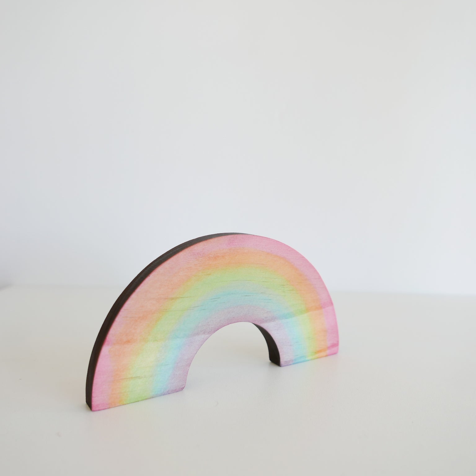 Wooden rainbow stacker in soft pastel colors, arranged in an arch on a plain white background