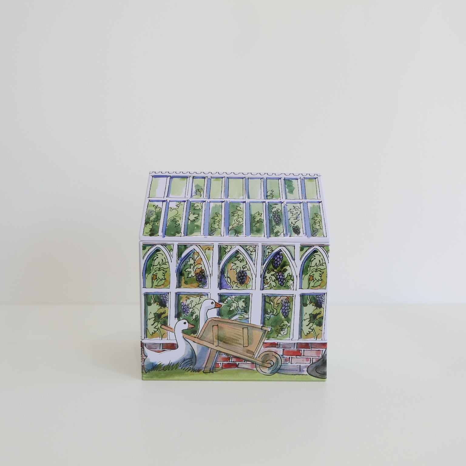 Small tin box with a decorative design of a garden scene, including a duck and a wheelbarrow, on a white background.