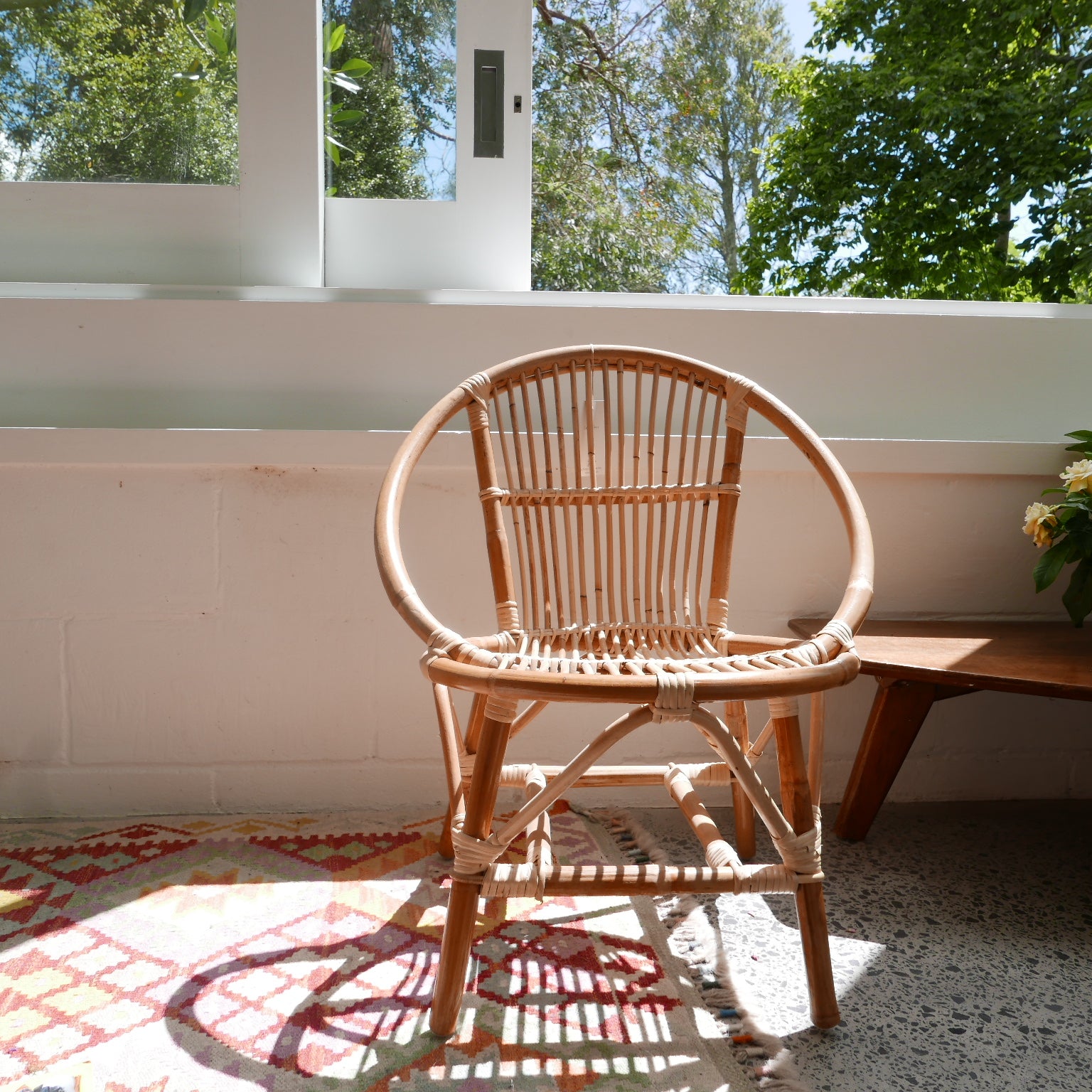 Wicker chair in a room with a large window and greenery outside