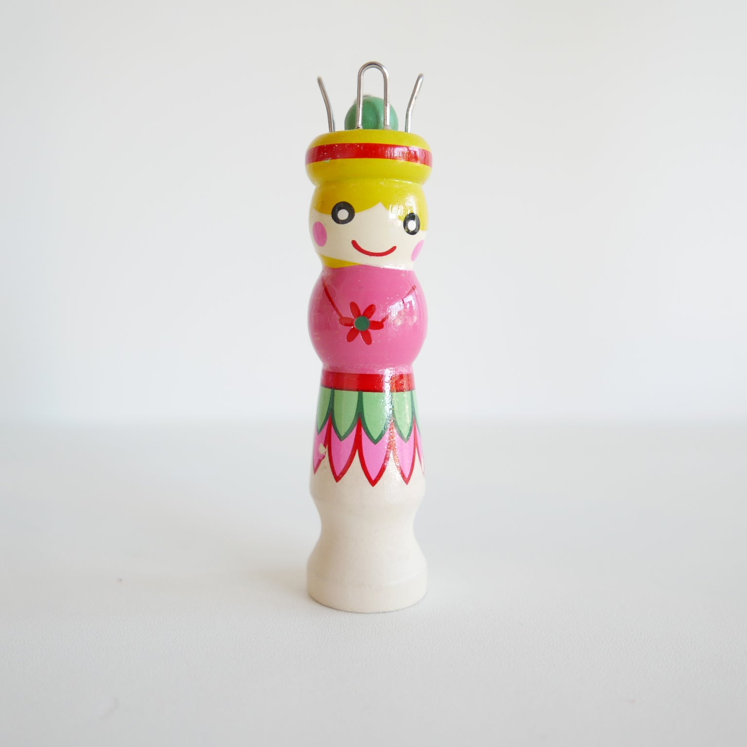 Cheerful wooden knitting dolly toy with painted face, photographed on a plain white background