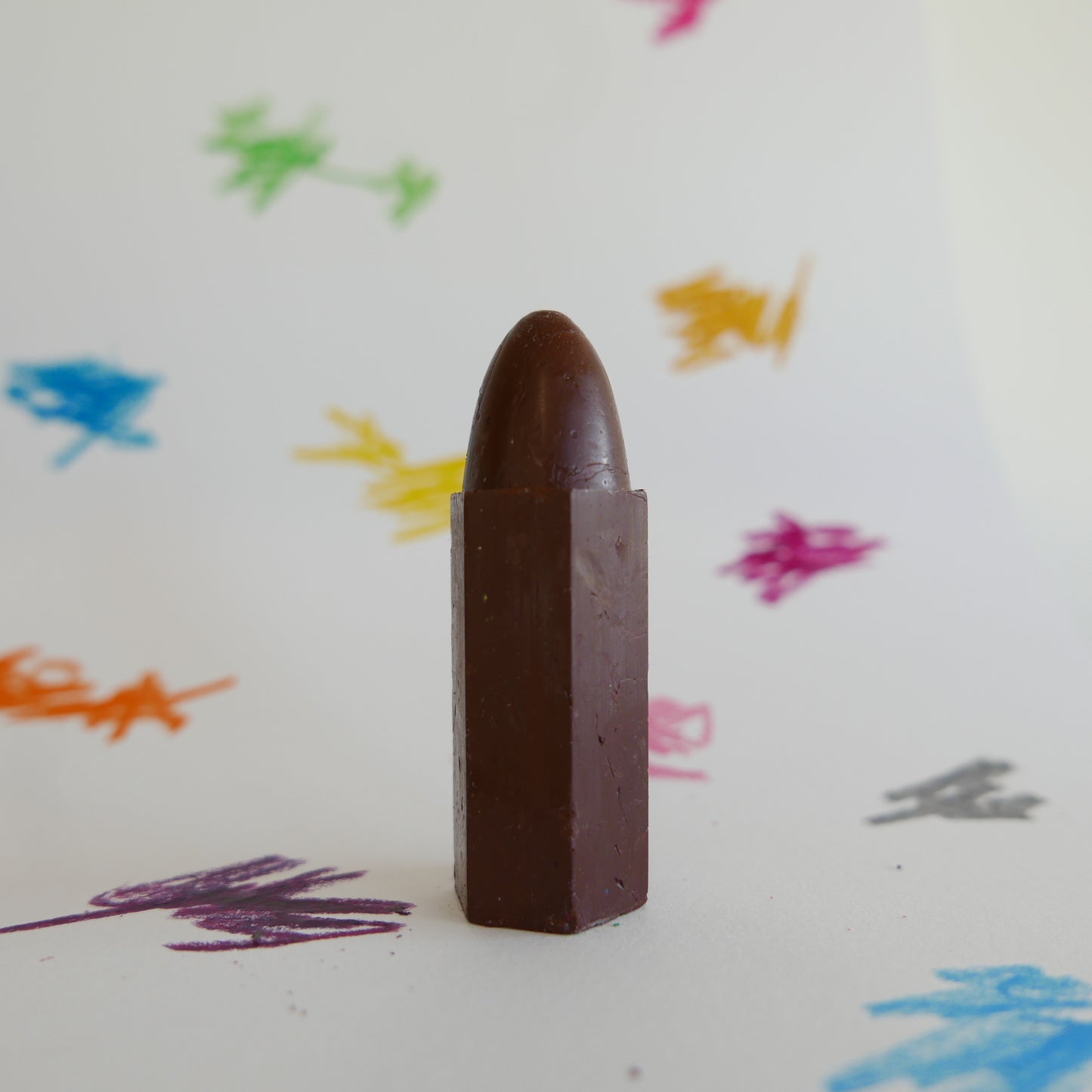 Chocolate brown crayon on a white background with colorful crayon marks