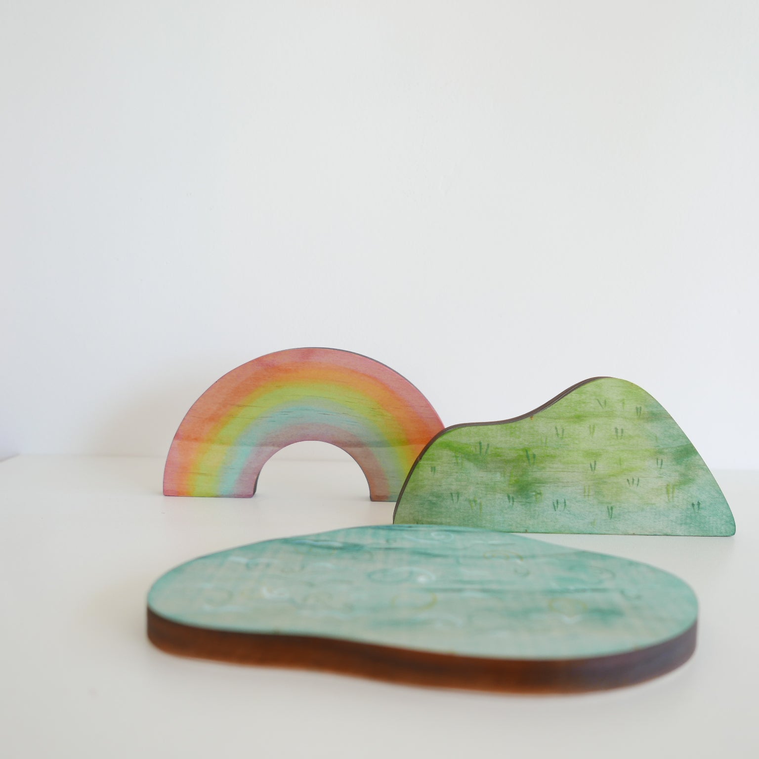 Wooden play set featuring a blue lake piece and a green grassy hill, arranged together on a white background