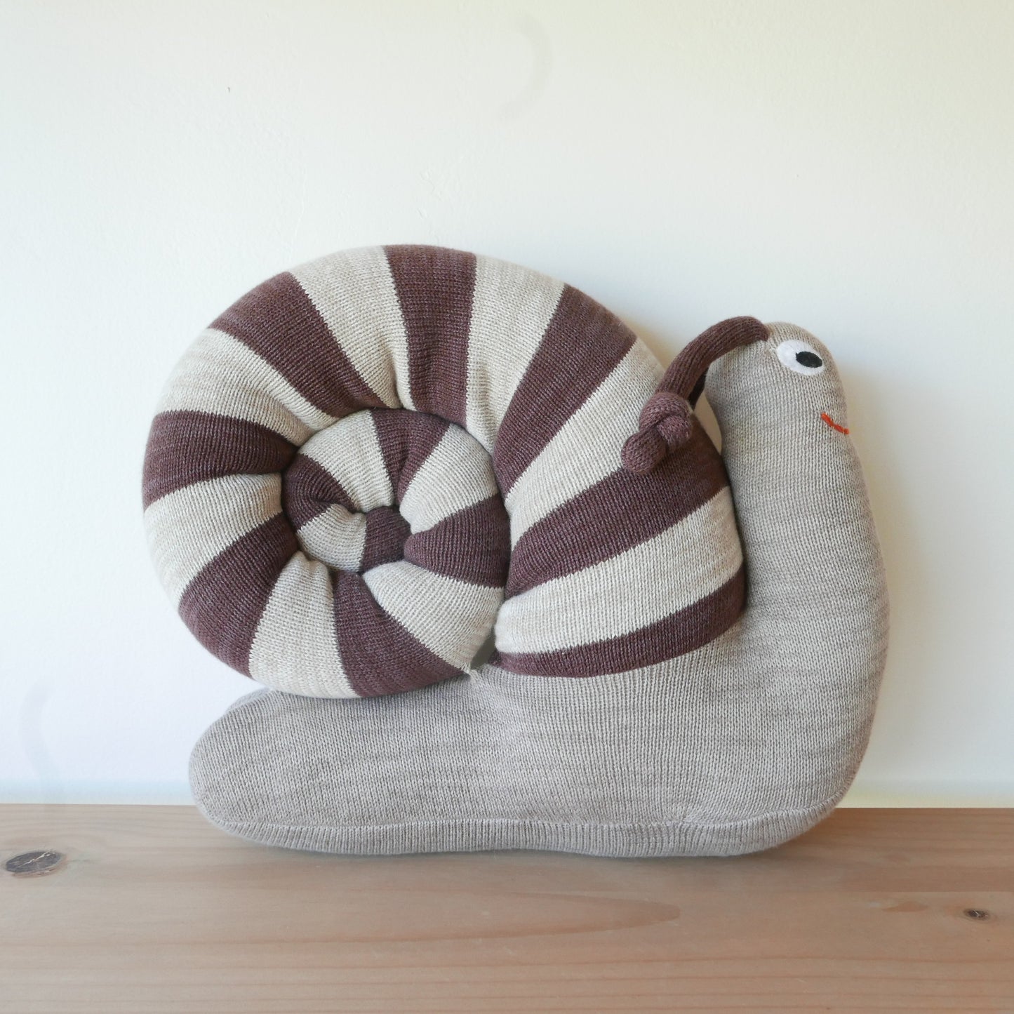 Knitted snail toy with striped shell on a wooden surface