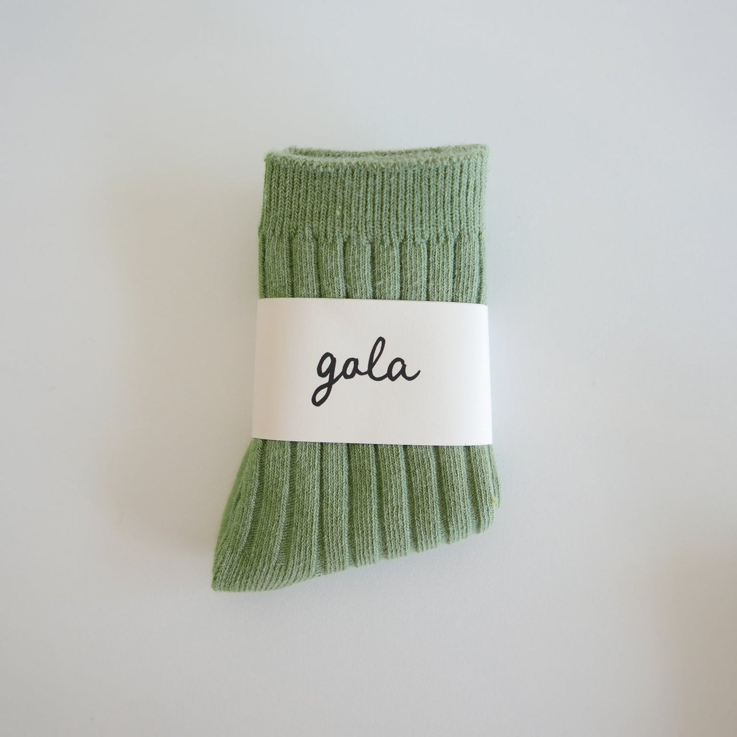 Folded green socks with a 'gala' label on a light gray background