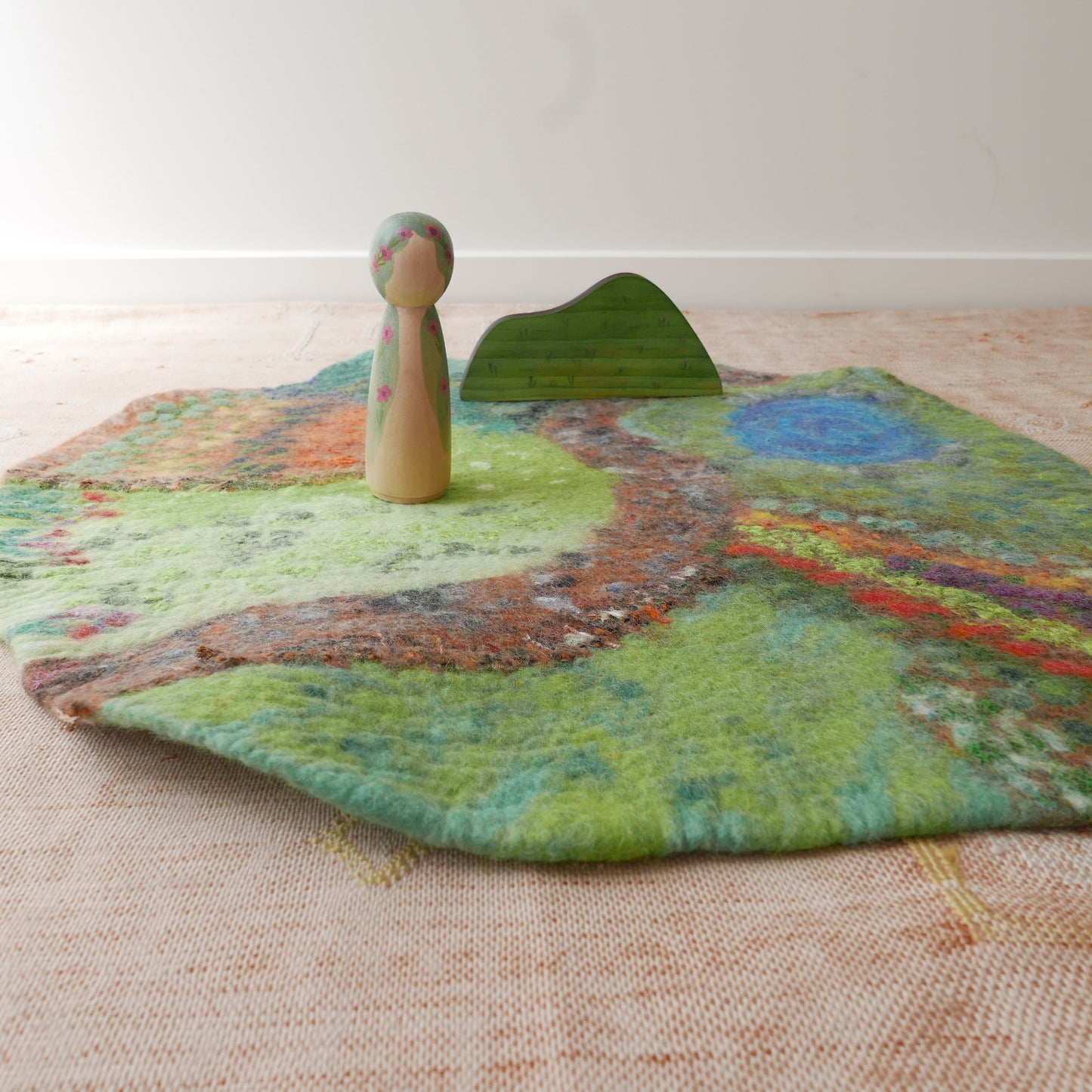 Colorful felted rug with a wooden peg and green leaf on a beige surface