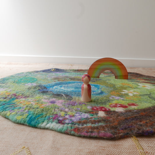 Felted rug with a colorful landscape, pond, rainbow, and wooden figure.