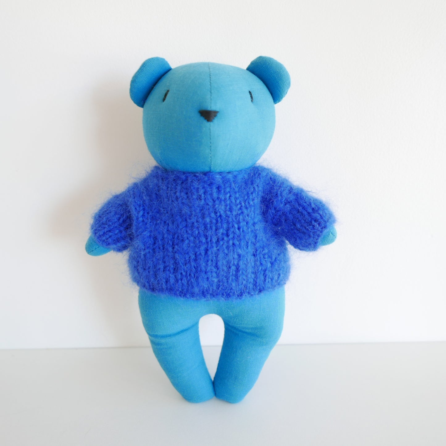 Blue teddy bear wearing a knitted sweater on a white background