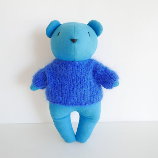 Blue teddy bear wearing a knitted sweater on a white background