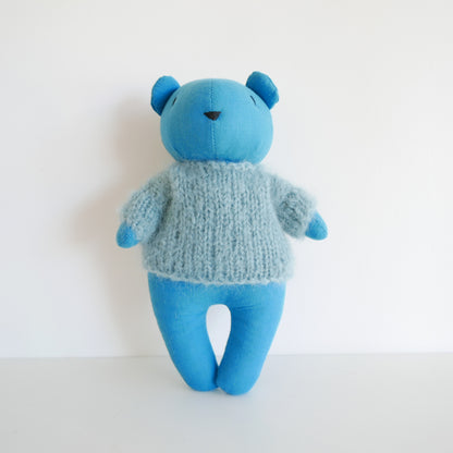 Blue teddy bear wearing a knitted sweater on a white background