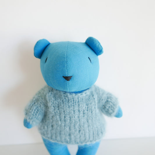 Blue teddy bear wearing a knitted sweater on a white background