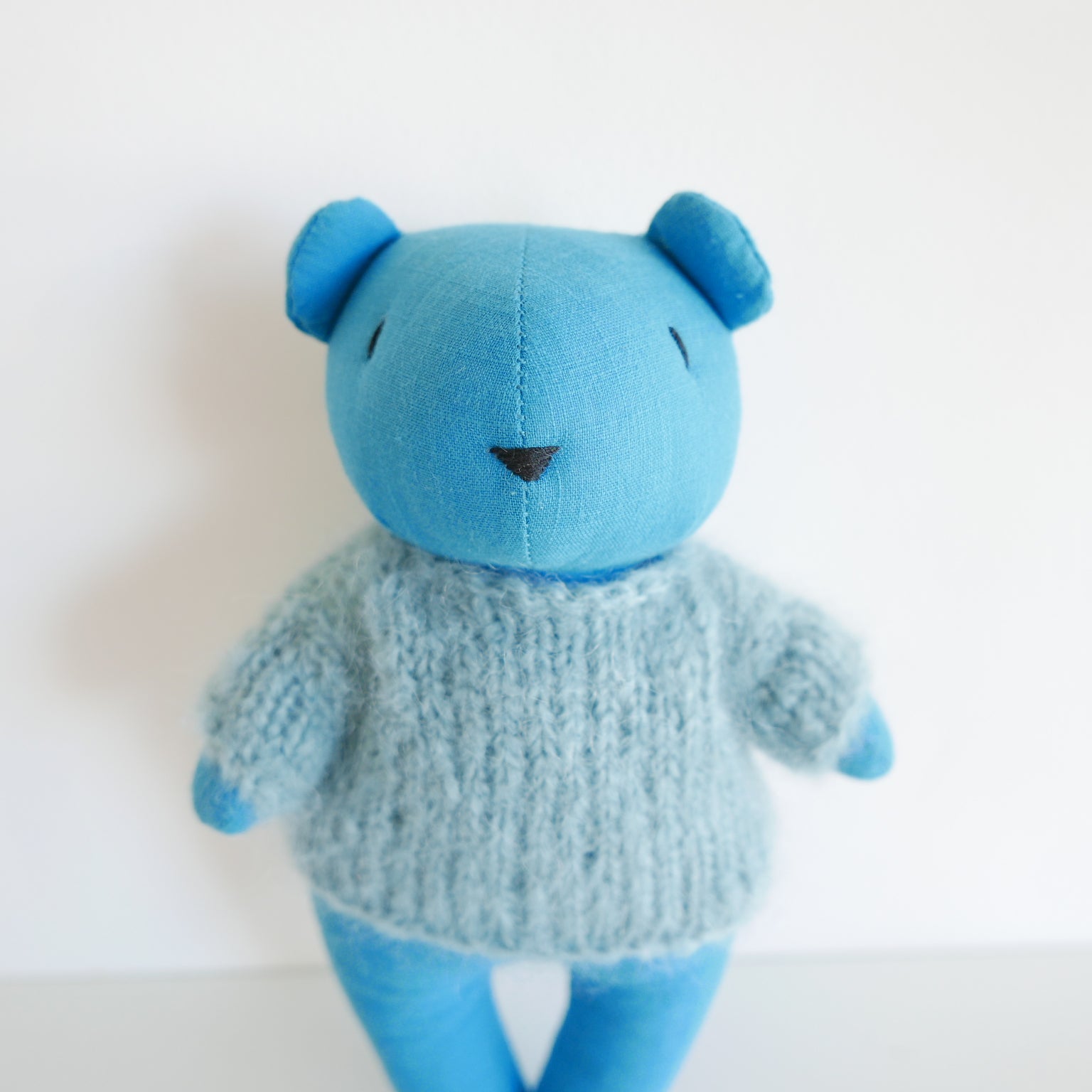 Blue teddy bear wearing a knitted sweater on a white background