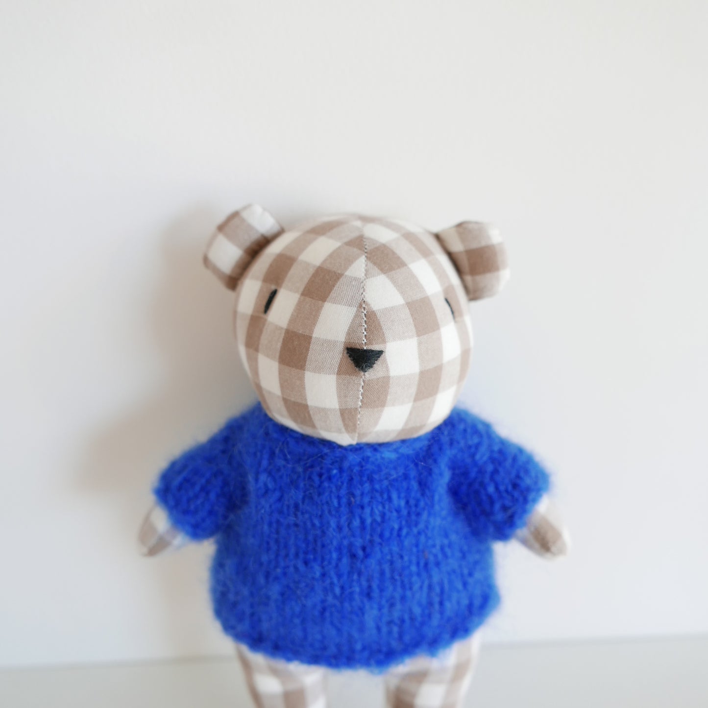 Small blue and checkered brown plush toy on a white background