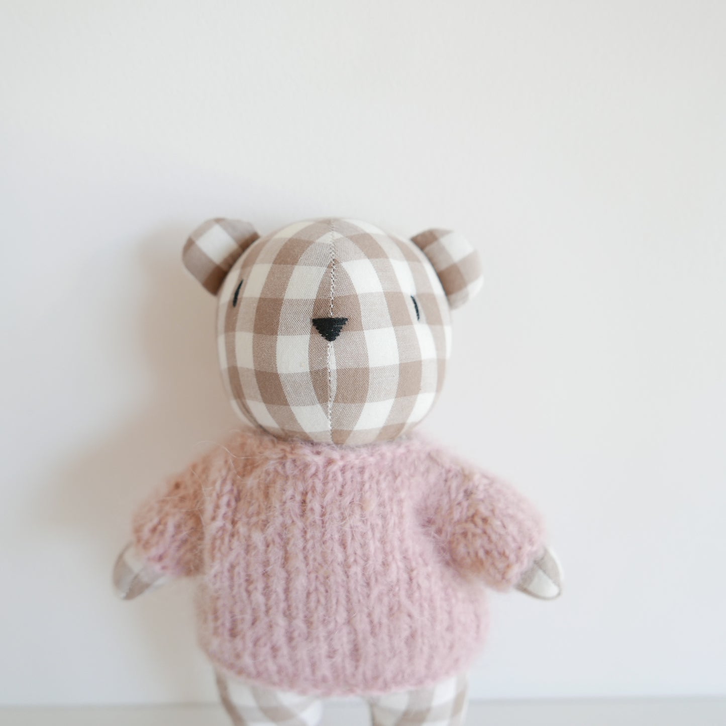 Stuffed animal toy with checkered head and pink outfit on a white background